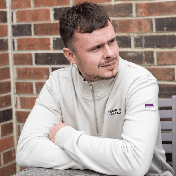 Man wearing a white jacket with logos sitting against a brick wall.