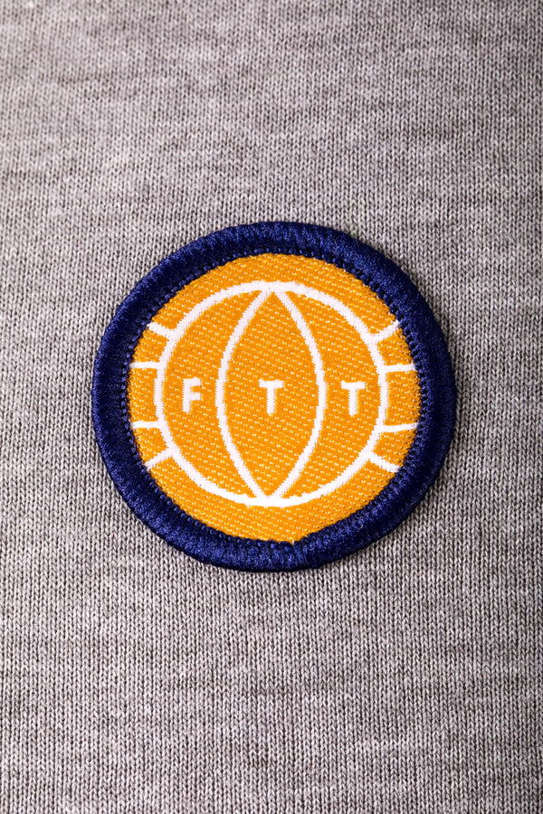 Circular patch with 'FTT' logo on a gray fabric background