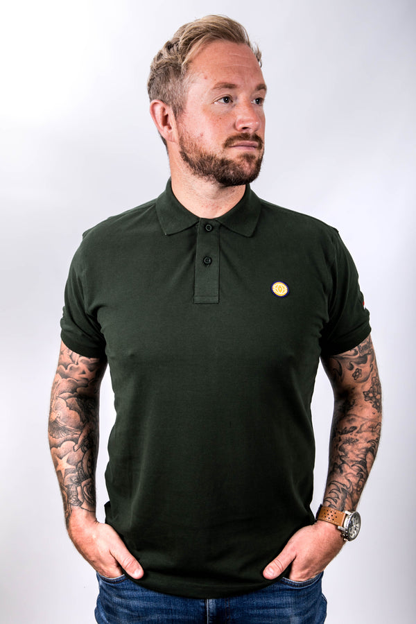 Man wearing a dark green polo shirt with a small yellow logo on a white background