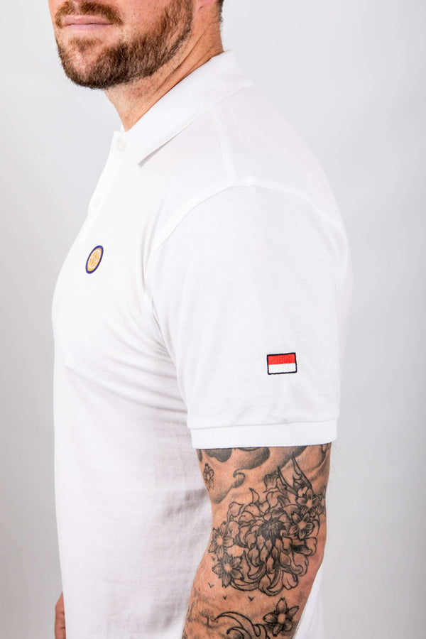 Man wearing a white polo shirt with small logos on a plain background