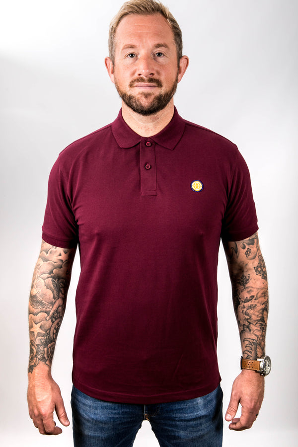 Man wearing a maroon polo shirt with a small yellow logo on a white background