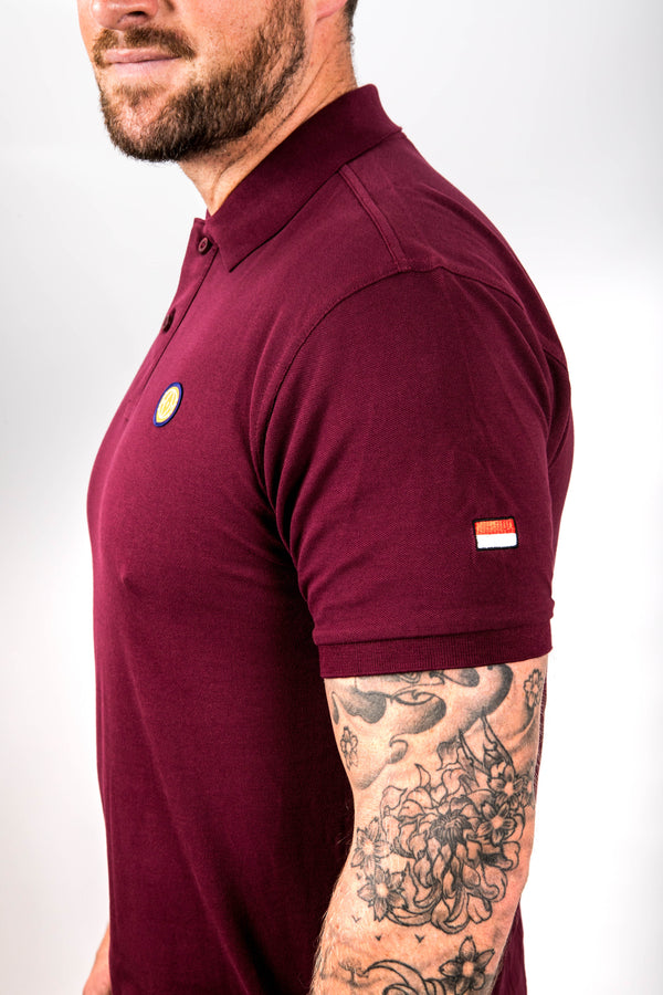 Man wearing a maroon polo shirt with a logo on a white background