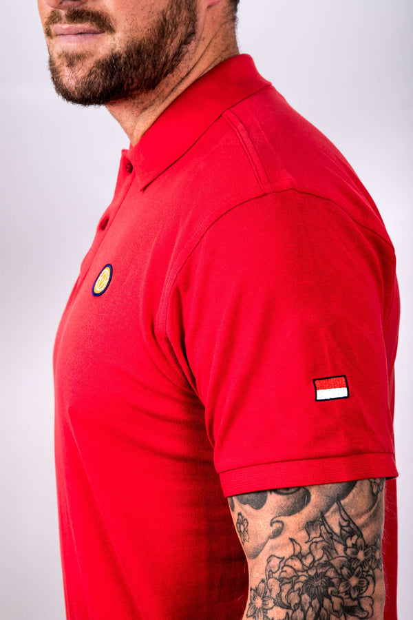 Person wearing a red polo shirt with a small flag on the sleeve against a plain background