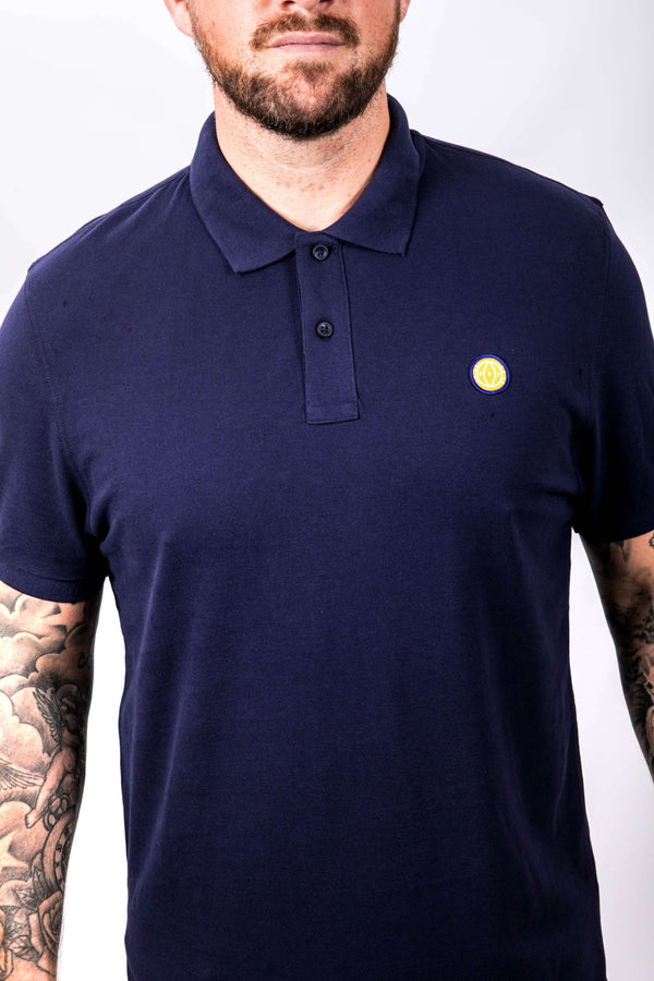 Man wearing a navy blue polo shirt with a yellow logo on a white background