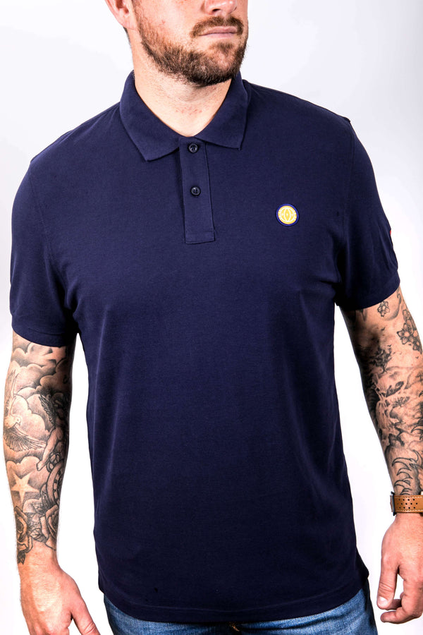 Man wearing a navy blue polo shirt with a small yellow logo on a white background