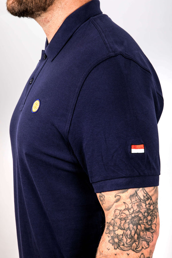 Navy blue polo shirt with a small yellow circle and red flag logo on a white background