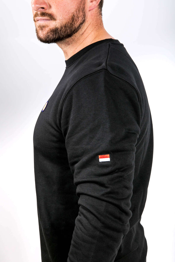 Person wearing a black long-sleeve sweatshirt with a small flag patch on a white background