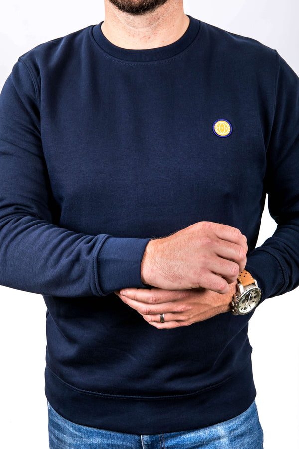 Person wearing a navy blue sweatshirt with a small yellow logo on a white background