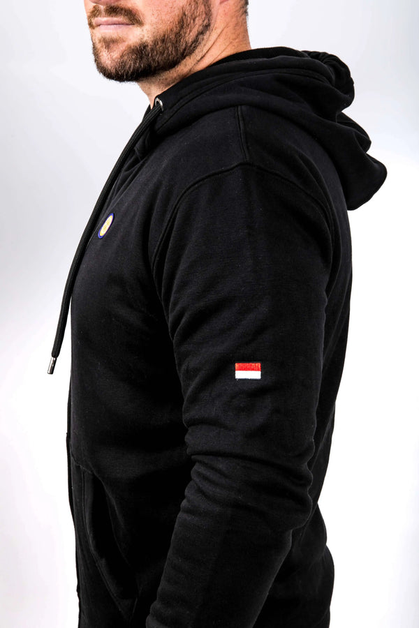 Person wearing a black hoodie with a small flag patch on the sleeve against a white background