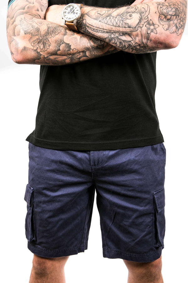 Person wearing a black t-shirt and navy cargo shorts with tattoos on arms.