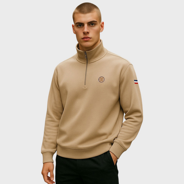 Man wearing a beige high-neck sweatshirt with a small logo on a plain background