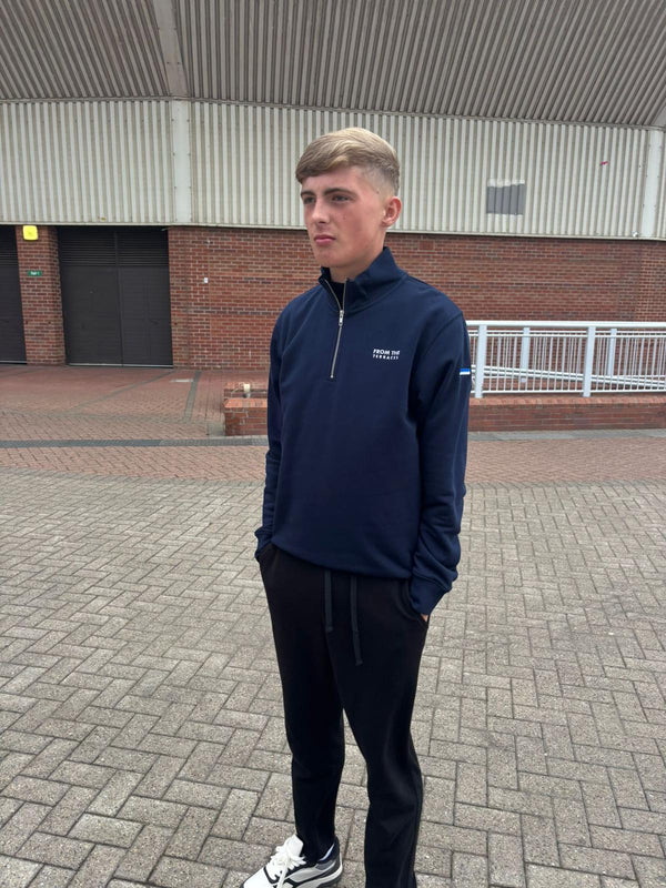 Man wearing a navy blue jacket with a logo on a paved area.