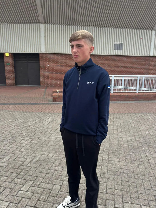 Man wearing a navy blue jacket with a logo on a paved area.