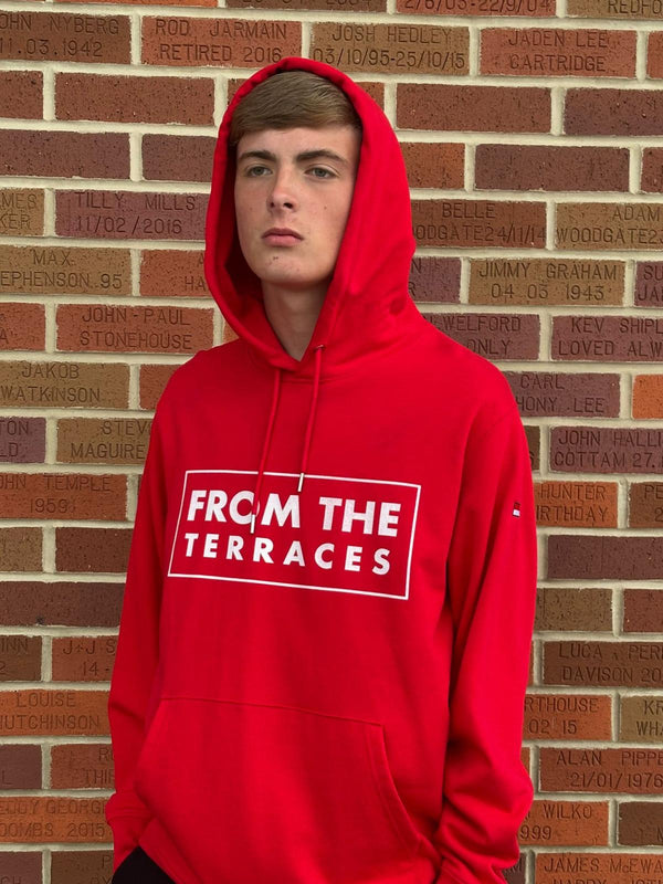 Person wearing a red hoodie with 'FROM THE TERRACES' text against a brick wall.