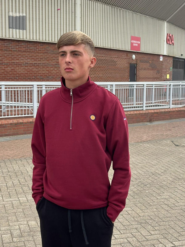 Person wearing a maroon pullover with a small logo, standing outdoors.