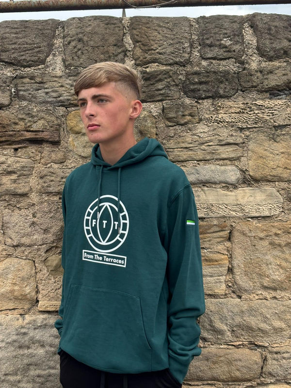 Person wearing a green hoodie with a logo against a stone wall