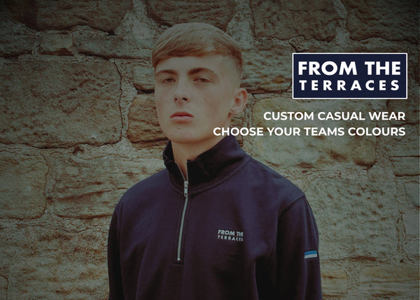 Person wearing a dark blue jacket with 'From the Terraces' branding against a stone wall.
