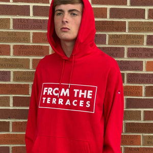 Person wearing a red hoodie with 'FROM THE TERRACES' text against a brick wall.