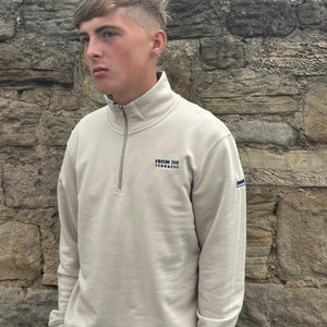 Person wearing a beige pullover with a logo against a stone wall