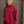 Person wearing a red pullover with a logo, standing against a brick wall.