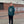 Person wearing a green hoodie with a logo standing on a brick pavement.