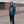 Person wearing a green hoodie with a logo, standing on a paved area with a building in the background.