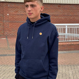 Person wearing a navy hoodie with a small yellow logo, standing outdoors.