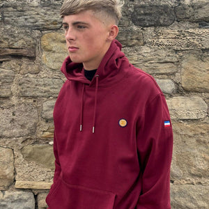 Person wearing a maroon hoodie with logos against a stone wall