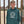 Person wearing a teal hoodie with a logo in front of a rusty metal gate.